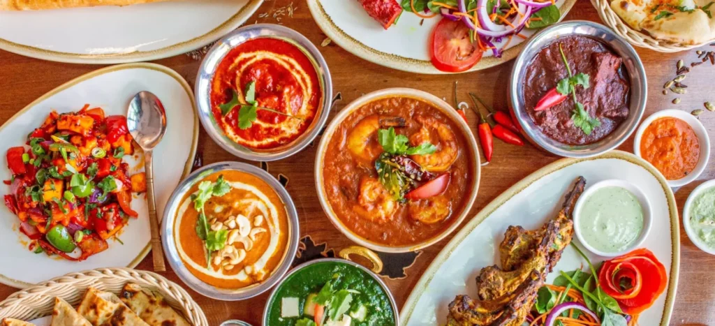 Overhead spread of authentic Indian dishes at Beyond India Adelaide including prawn curry, korma, palak paneer, lamb skewers, vegetable stir fry, chutneys and naan bread